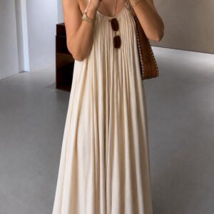 Détail d'une robe longue écrue plissée à fines bretelles avec coupe ample et tissu fluide.